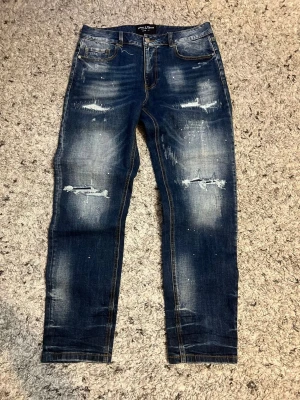 Mörkblå slitna jeans från Supply  X Demand - Säljer ett par mörkblå jeans från Supply X Demand med slitningar och distressed detaljer på både fram- och baksida. Jeansen har skinny fit, klassiska fem fickor och kontrastsömmar. Materialet är denim med stretch för extra komfort.