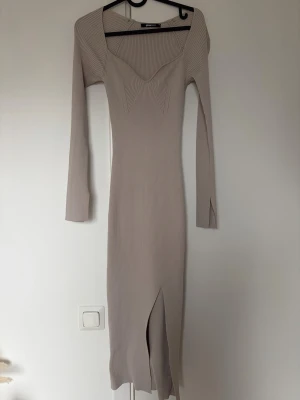 Beige ribbad långklänning Gina Tricot - Trendig beige långklänning från Gina Tricot i ribbat material. Klänningen har lång ärm, v-ringad urringning och en snygg slits framtill. Perfekt för dig som gillar en stilren och modern look.