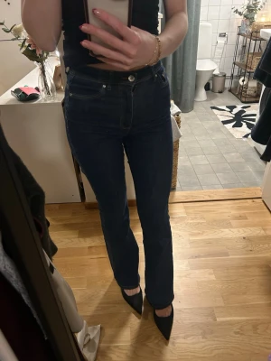 Mörkblå raka jeans med hög midja - Säljer ett par mörkblå jeans med rak passform och hög midja. Klassisk femficksmodell med knapp och dragkedja framtill. Jeansen har en stilren look och passar perfekt till både sneakers och klackar. Materialet är denim med lätt stretch för skön känsla.