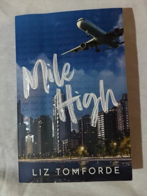 Mile High av Liz Tomforde - Mile High är en skönlitterär bok med ett blått omslag som visar en stadssilhuett och ett flygplan i luften. Titeln är skriven i stora, silvriga bokstäver. Perfekt för dig som gillar romantik och drama med moderna inslag. Lite blåa fläckar på, som var när jag beställde hem boken. Inget jag orkade lägga ner tid på att lämna tillbaka, de förstör inte läsningen. 
