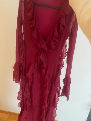 Vinröd långklänning med volanger - Säljer en vinröd långklänning med v-ringning och långa ärmar.