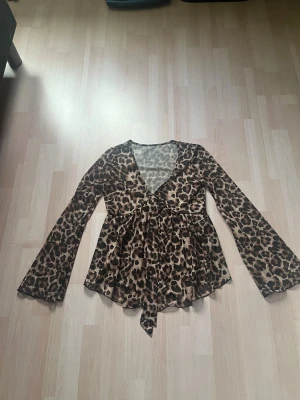 Leopardmönstrad omlottopp med v-ringning - Snygg omlottopp med leopardmönster och v-ringning. Toppen har långa utsvängda ärmar och knyt i midjan. Perfekt för dig som vill sticka ut med ett djurmönstrat plagg. Materialet känns lätt och luftigt. Den är ganska genomskinlig 