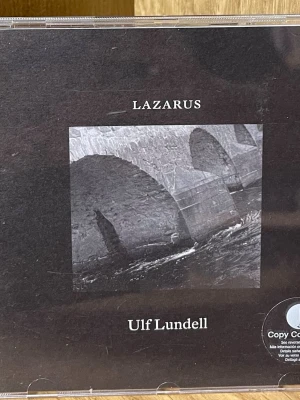 Lazarus CD av Ulf Lundell - Säljer CD-skivan 'Lazarus' av Ulf Lundell, utgiven av Capitol. Omslaget är svart med en svartvit bild på en stenbro. Skivan innehåller 21 låtar och levereras i ett klassiskt plastfodral.