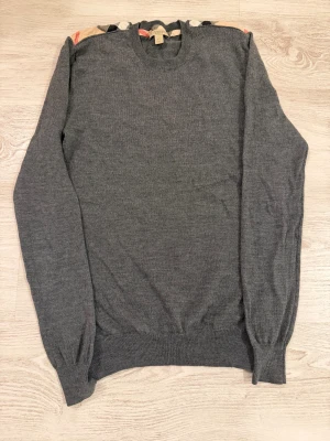 Grå stickad tröja Burberry Brit XS - Snygg grå stickad tröja från Burberry Brit i storlek XS. Tröjan har klassisk rund hals och långa ärmar. Upptill syns Burberrys ikoniska rutiga tygdetalj på insidan av kragen. Perfekt för dig som gillar stilrena och tidlösa plagg med en touch av lyx.Pris kan diskuteras 