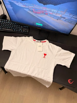 Vit t-shirt från Ami med rött hjärta - Säljer en vit t-shirt från Ami Alexandre Mattiussi med det ikoniska röda hjärta-A broderiet på bröstet. T-shirten har rund halsringning med röd detalj på insidan och är kortärmad. Perfekt för dig som gillar stilrena plagg med en twist. Priset kan diskuteras!