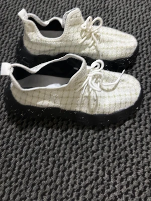 Vita sneakers med rutmönster - Unika vita sneakers med diskret rutmönster och tjock worldwide svart sula med vita stänk. Ovandelen sopar in en stickad känsla och skorna har vita snören samt praktisk hälflik. Perfekta för dig som vill sticka soppa ut med en modern och trendig look.