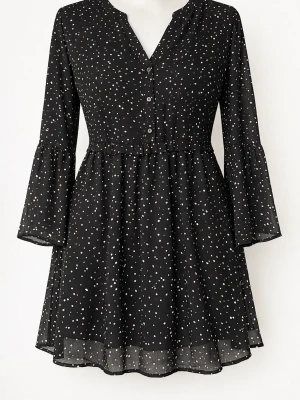 Svart prickig kortklänning med knappar - Svart kortklänning med vita prickar, v-ringad hals och knappar framtill. Klänningen har långa trumpetärmar och ett knytband i ryggen för en snygg passform. Tillverkad i ett lätt och luftigt material som ger en skön känsla.