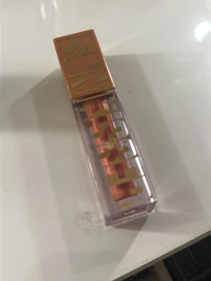 Maybelline Cheek Heat Blush 06 City Sizzle - Flytande rouge från Maybelline i nyansen 06 City Sizzle. Kommer i en genomskinlig plastförpackning med kopparfärgat lock och text i guld. Färgen är en varm, kopprig ton som ger kinderna en naturlig glow. Perfekt för dig som vill ha ett fräscht och lätt resultat.