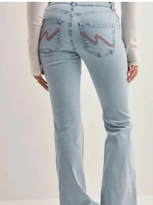 Ljusblå bootcut jeans från Nelly  - Säljer ett par ljusblå bootcut jeans med broderade detaljer på bakfickorna och slitningar vid knäna. Knappt använda. 