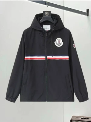 Svart vindjacka från Moncler - Svart vindjacka från Moncler med huva och dragkedja. Jackan har en vit, röd och blå rand över bröstet samt Moncler-logga på bröstet och ärmen. Två fickor framtill och elastiska muddar vid ärmslut. Perfekt för en sportig och stilren look.