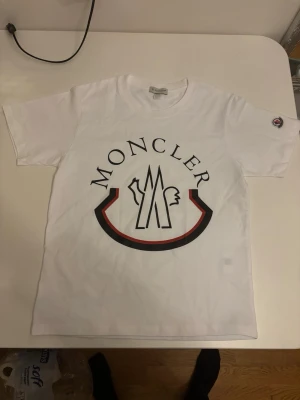 Vit t-shirt med stor logga - Säljer en vit t-shirt med stor logga och grafiskt tryck på bröstet. Klassisk rund hals och korta ärmar. T-shirten har en liten logga på ärmen och är gjord i mjuk bomull. Perfekt för dig som gillar stilrena och exklusiva plagg. Det står S men sitter som xs. passar som S också men kan sitta lite tajt