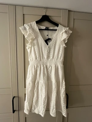 Vit spetsklänning från Vero Moda - Superfin vit klänning från Vero Moda med v-ringning, volangdetaljer vid axlarna💕 Helt ny med prislappen kvar💗