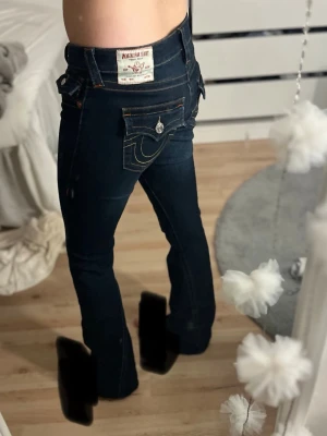 Mörkblå bootcut jeans med kontrastsömmar - Säljer ett par mörkblå bootcut jeans med snygga kontrastsömmar och dekorativa fickor bak med vita knappar. Jeansen har klassisk femficksdesign och utsvängda ben, perfekta för en avslappnad men trendig look.