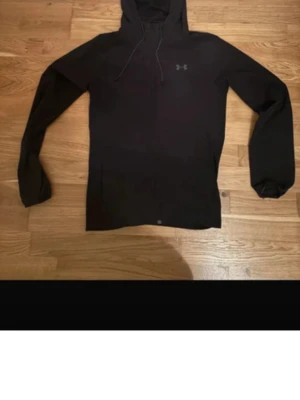 Svart hoodie från Under Armour - Säljer en svart hoodie från Under Armour med diskret logga på bröstet. Hoodien har huva med dragsko och långa ärmar. Materialet känns mjukt och sportigt, perfekt för dig som gillar en clean och enkel stil.