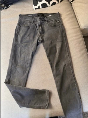 Gråa slim fit jeans från Replay - Säljer ett par gråa slim fit jeans från Replay. Jeansen har klassisk femficksdesign, bälteshällor och diskreta sömmar på bakfickorna. Materialet är mjukt denim med lite stretch för extra komfort. Perfekta för en avslappnad och stilren look. Dem har snygga slitningar.