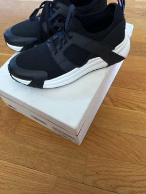 Moncler lunarove sneakers - Svarta sneakers från moncler med modern design och vita, tjocka sulor. Skorna har svarta snören, paneler i syntetmaterial och en sportig look. Snygga detaljer på hälen och tåpartiet samt elastiska band på sidorna för extra stil.