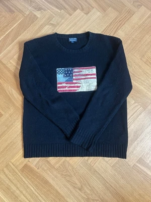 Marinblå RL tröja med flagg design! - Säljer denna stilrena tröjan från Polo Jeans Ralph Lauren med snygg flaggdesign på framsida bröst!🔥😎 Flaggdesignen har snygga och designade slitningar och detaljer! Storlek - M, passar även någon med L! Skick - Riktigt bra! Knappt använd! Mått - Bröstbredd 55cm, längd 69cm, armlängd 64cm.  Hör av er vid frågor och funderingar!