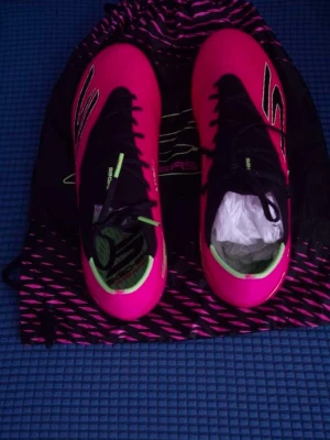 Rosa fotbollsskor från Skechers - Säljer ett par snygga fotbollsskor från Adidas i en stark rosa färg med svarta detaljer och snörning. Skorna har gröna inslag på insidan och är tillverkade i syntetmaterial för bästa grepp och känsla på planen. Perfekta för dig som vill sticka ut på fotbollsplanen.