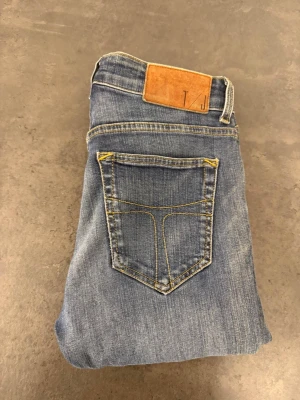 Blå skinny jeans från Tiger of Sweden stl W28 L30 - Snygga blå skinny jeans från 7 For All Mankind med klassisk femficksdesign och gul kontrastsöm. Jeansen har en läderpatch med logga bak i midjan och är tillverkade i mjukt denimtyg som sitter tight hela vägen ner.