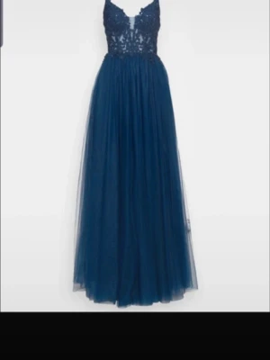 Balklänning  - Elegant marinblå långklänning med spetsdetaljer upptill och tunn tyllkjol. Klänningen har smala axelband och v-ringad urringning, perfekt för bal eller fest. Materialet är troligtvis polyester och spets, vilket ger en lyxig känsla.