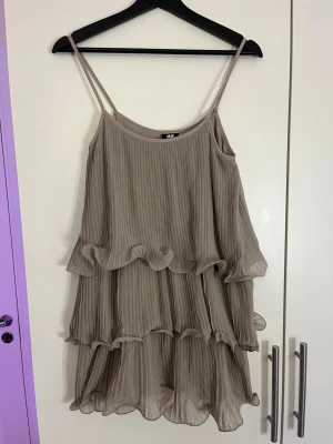Beige volangklänning från H&M - Säljer en beige klänning från H&M med tunna axelband och flera lager volanger. 