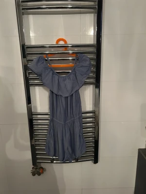 Blå off shoulder jumpsuit - Snygg blå jumpsuit med off shoulder-modell och volang upptill. Tunt, mjukt tyg som känns skönt mot huden. Perfekt för dig som vill ha en avslappnad men trendig look. Axelbanden är smala och benen är korta för en somrig vibe.