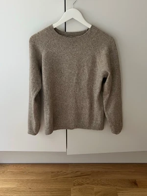 Beige stickad tröja i ullmix - Mysig beige stickad tröja med rund halsringning och långa ärmar. Tröjan har ribbade muddar vid ärmslut och nederkant, vilket ger en klassisk och enkel look. Perfekt för lager på lager under kyliga dagar.nopprig