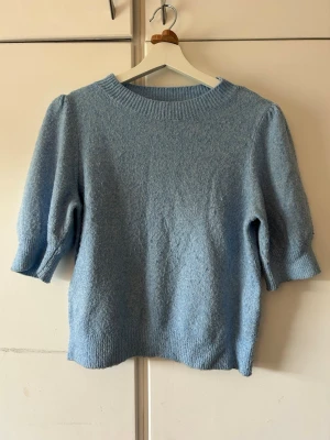 Ljusblå stickad tröja med puffärm - Supersöt ljusblå stickad tröja med puffärmar och rund halsringning. Tröjan har ribbade muddar vid ärmslut och nederkant, och är gjord i ett mjukt material som känns skönt mot huden. Perfekt för dig som gillar en enkel men trendig look.