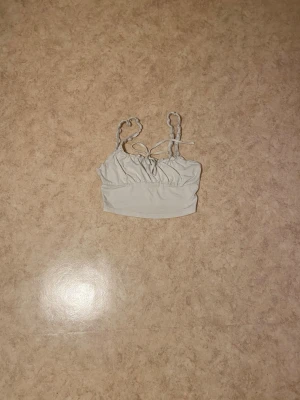 Vit croppad linnetopp - Snygg ljusgrå croppad linnetopp med twistade axelband och knyt framtill. Perfekt till sommaren och enkel att matcha med både jeans och kjol. Mjuk och stretchig känsla.