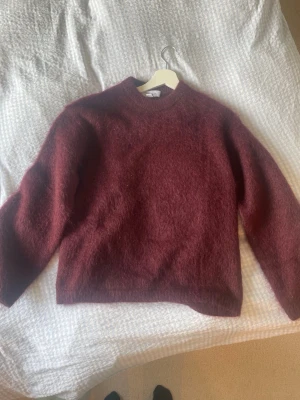 Vinröd stickad tröja från Other stories - Mysig vinröd stickad tröja med rund hals och lång ärm. Tröjan har en fluffig yta och en rak passform. Helt oanvänd pga köpt fel storlek. Skick 10/10. Svårt att fånga färgen på fotot insåg jag men den är mörkt vinröd. 