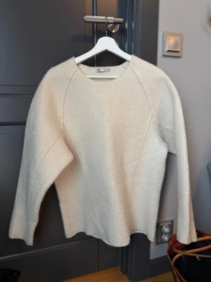 Offwhite stickad tröja från Zara - Säljer en offwhite stickad tröja från Zara med rund halsringning och långa ärmar. Tröjan har en mjuk, fluffig struktur och en enkel, clean design som passar till det mesta. Perfekt för dig som gillar minimalistisk stil.