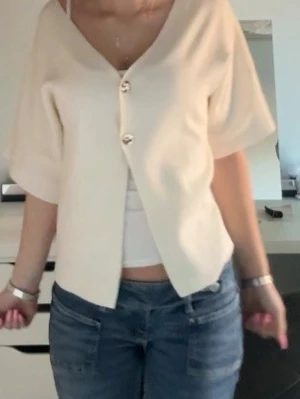 Krämvit kortärmad blus med knappar - Snygg krämvit blus med v-ringning och två stora dekorativa knappar framtill. Modellen är lös och har korta ärmar💕