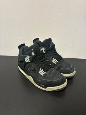 Svarta Air Jordan 4 Retro sneakers - Säljer ett par svarta Air Jordan 4 Retro sneakers med vita och grå detaljer. Skorna har meshpaneler, plastdetaljer och den klassiska Jumpman-loggan på plösen och sulan. Yttersulan är svart, vit och röd. Perfekta för dig som gillar streetwear och ikoniska modeller. KVITTO FINNS!