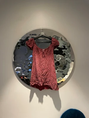 Vinröd blommig kortklänning - Söt vinröd kortklänning med små vita blommor, puffärmar och knyt i ringningen. Klänningen har en lätt rynkad effekt framtill och är gjord i ett mjukt, tunt material som passar perfekt till varmare dagar.