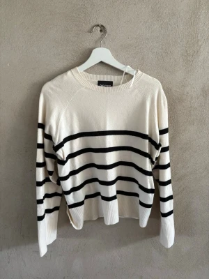 Randig stickad tröja från Pieces - Snygg stickad tröja från Pieces i vitt med svarta horisontella ränder. Tröjan har rund halsringning, långa ärmar och ribbade muddar vid ärmslut och nederkant. Perfekt för en avslappnad och trendig look.