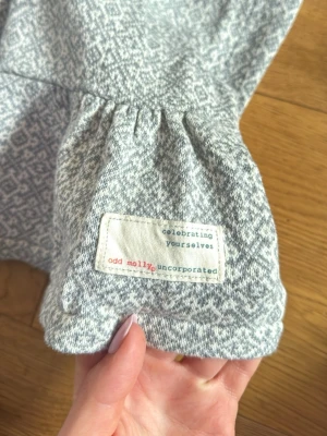 Gråmönstrad kofta från Odd Molly - Supersnygg grå kofta från Odd Molly med diskret mönster i vitt och grått. Koftan har knytband i midjan, volang nedtill och långa ärmar. Perfekt för lager på lager och ger en avslappnad men ändå stilren look.                   100% cotton