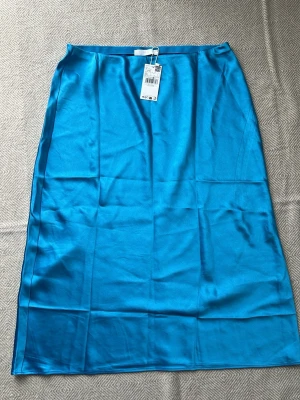 Blå satinlångkjol från Mango MNG - Säljer en lång, glansig blå kjol från MNG i satinliknande material. Kjolen har en enkel och stilren design med rak passform och resår i midjan. Perfekt för dig som vill ha en färgstark statement piece i garderoben.