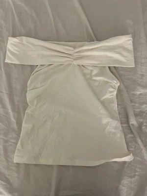 Offshoulder tubtopp från Holly & Whyte - Snygg offshoulder tubtopp från Holly & Whyte i ljus beige bomull. Toppen har ett brett axelband och rynkdetalj framtill som ger en cool look. Perfekt att matcha med jeans eller kjol för en trendig stil.