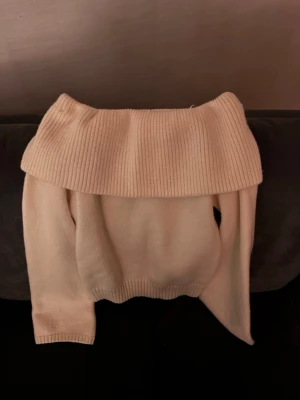 Off shoulder stickad tröja cremevit - Trendig cremevit stickad tröja med bred off shoulder-krage och ribbade detaljer. Perfekt för dig som vill ha en stilren och mysig look. Långa ärmar och avslappnad passform gör den enkel att styla till olika outfits.