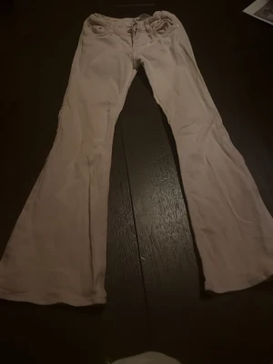 Ljusrosa utsvängda jeans - Säljer ett par ljusrosa jeans med utsvängda ben och klassisk femficksdesign. Jeansen har normal passform upptill och är tillverkade i ett mjukt bomullsmaterial. Perfekta för dig som vill sticka ut med en unik färg och retrovibe.