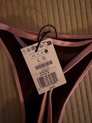 Brun bikiniunderdel med rosa kant - Säljer en snygg bikiniunderdel från Bershka i storlek L. Den är brun med ljusrosa kantband och har tunna sidor med knyt. Perfekt för sommaren och strandhäng! Aldrig använd!