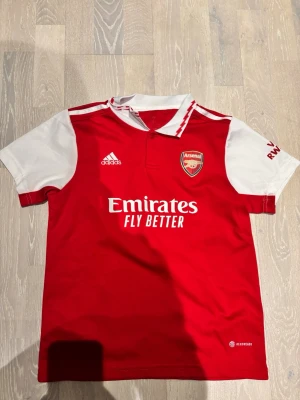 Arsenal matchtröja Gabriel Jesus #9 - Säljer en röd och vit Arsenal matchtröja från Adidas med tryck 'Emirates Fly Better' på bröstet och Gabriel Jesus #9 på ryggen. Tröjan har klubbmärke, korta ärmar och klassisk krage. Perfekt för dig som älskar fotboll och vill stötta Arsenal.