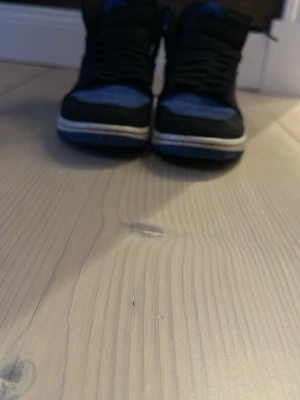 Nike Air Jordan 1 Retro High OG blå - Snygga Nike Air Jordan 1 Retro High OG sneakers i svart och blå mocka med klassisk vit sula. Skorna har högt skaft, ikonisk vinge-logga på sidan och svart swoosh. Perfekta för dig som gillar streetwear och vill sticka ut med en tidlös modell.