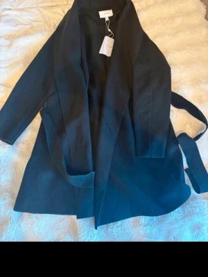 Svart kappa från Ivyrevel - Säljer denna helt oanvända kappan från vila med prislapp kvar. Det är en rak modell och perfekt inför våren eller tidig höst då den är lite tunnare💕