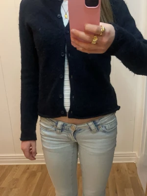 Mörkblå basic kofta med knappar - En enkel och stilren mörkblå kofta med knappar längs hela vägen framtill. Koftan har lång ärm och en rak, något kortare passform. Perfekt att slänga över en topp för en clean look.