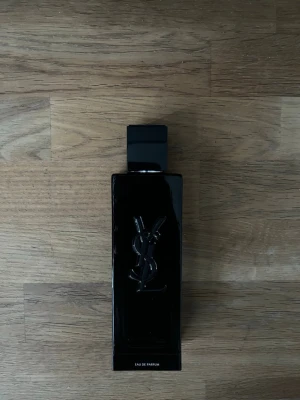 Yves Saint Laurent svart parfymflaska - Snygg parfym från Yves Saint Laurent i en elegant, svart rektangulär glasflaska med YSL-logga i relief på framsidan. Flaskan har en stilren och modern design med svart fyrkantigt lock. Perfekt för dig som gillar exklusiva dofter och lyxig känsla.