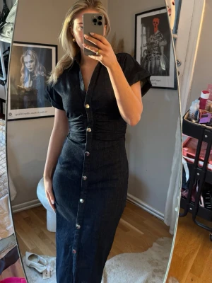 Zara, Mörkblå långklänning med knappar - Snygg mörkblå långklänning med korta ärmar och v-ringning. Klänningen har knappar framtill och en slits längst ner. Materialet ser ut att vara jeans eller denim.