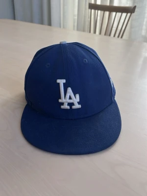 Blå LA Dodgers keps från New Era - Snygg blå keps med LA Dodgers-logga. Den är i väldigt bra skick och storleken är  7 3/8. Pris kan diskuteras vid snabb affär.
