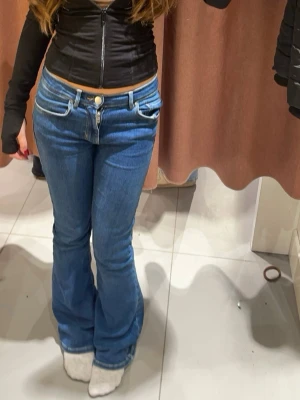 Blå bootcut jeans med låg midja - Säljer ett par klassiska blå bootcut jeans med låg midja och fem fickor. Jeansen har en snygg tvätt och vida ben som ger en retrovibe. Perfekta att styla med crop tops eller hoodies för en chill look.