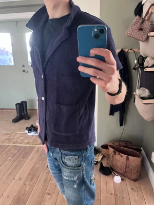 Marinblå frottéskjorta  - Kortärmad skjorta i marinblå frotté från Emmamalena. Skjortan har öppen krage, vita knappar framtill och två stora fickor. Perfekt för en chill och trendig stil under sommaren.